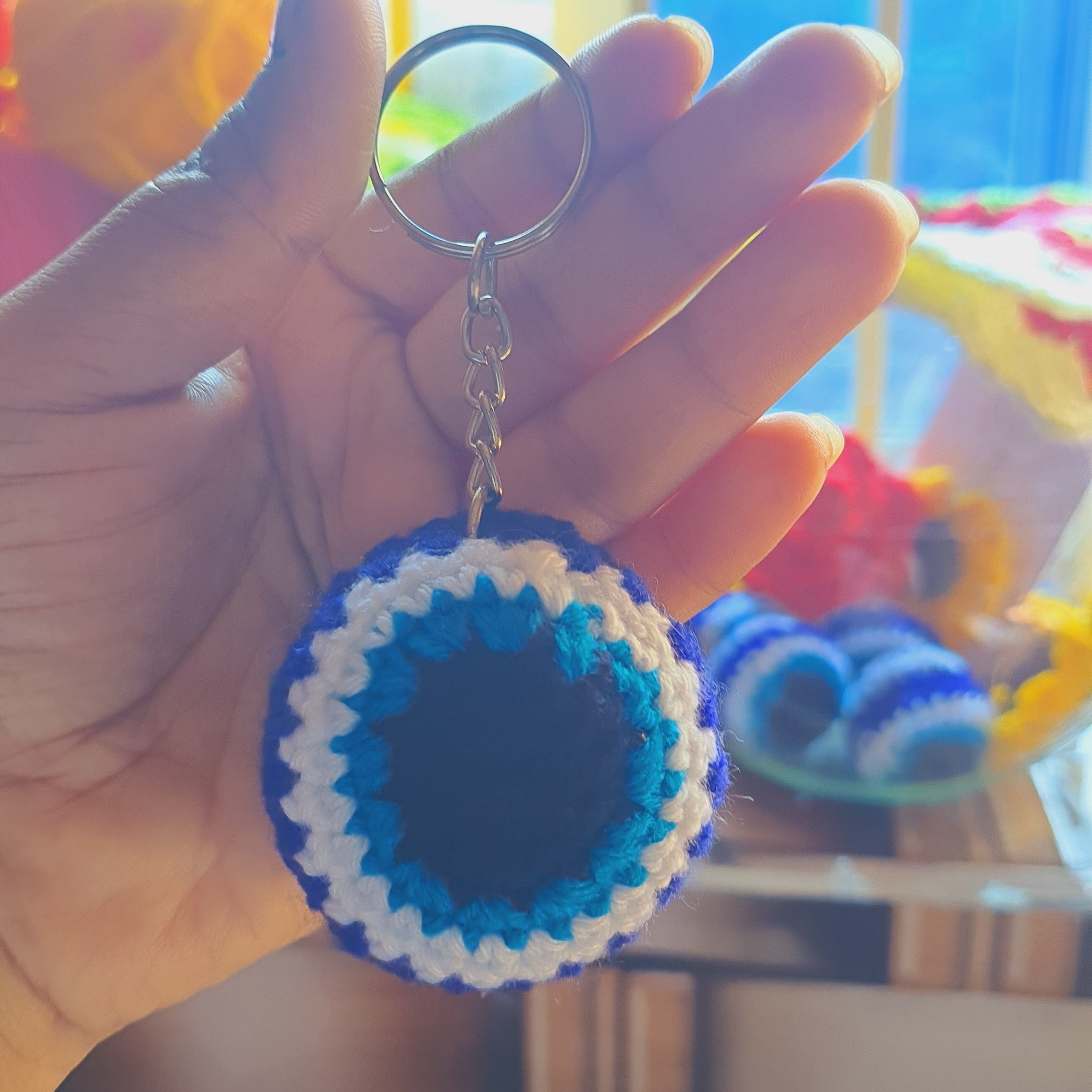 Hand holding a evil eye crocheted keychain in the background